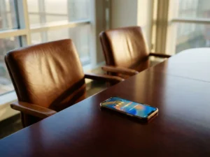 Smartphone mit bunter Feedback-Umfrage auf poliertem Konferenztisch neben leeren Lederstühlen bei warmem Tageslicht